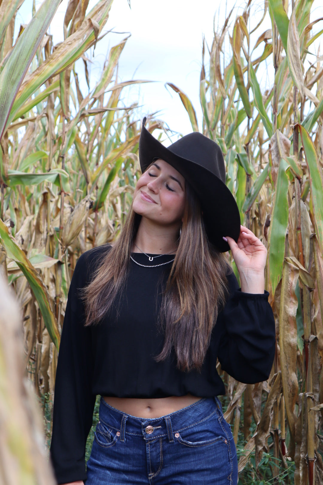 Person wearing a black hat and blue jeans standing among tall grass.