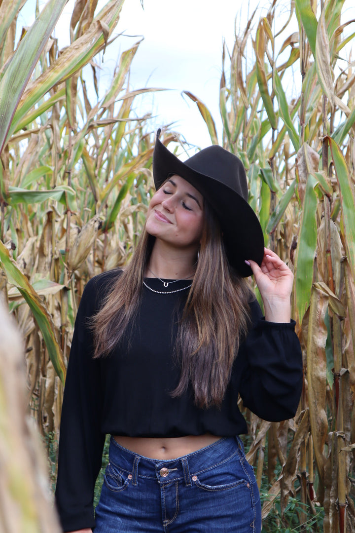 Person wearing a black hat and blue jeans standing among tall grass.