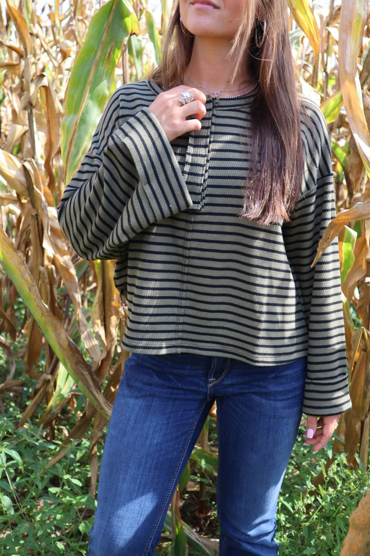 Person wearing a striped sweater and blue jeans standing in a cornfield
