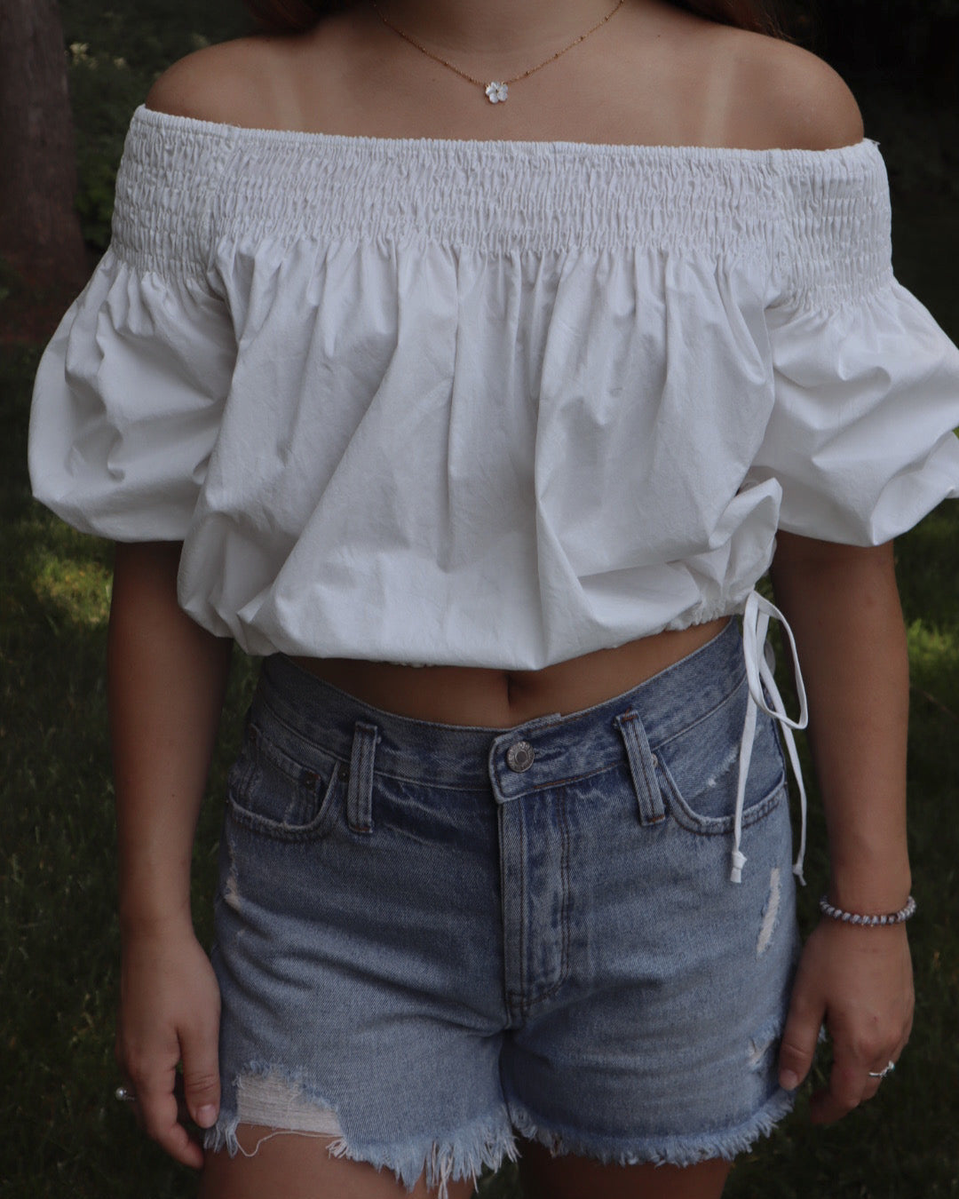 Person wearing a white off-shoulder top and denim shorts outdoors.