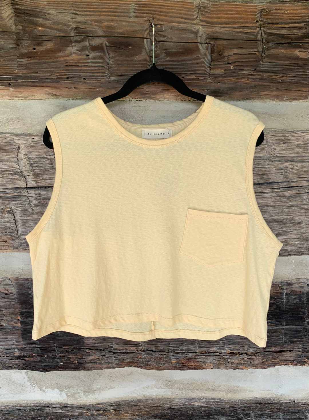 yellow sleeveless top on a hanger against a wooden background