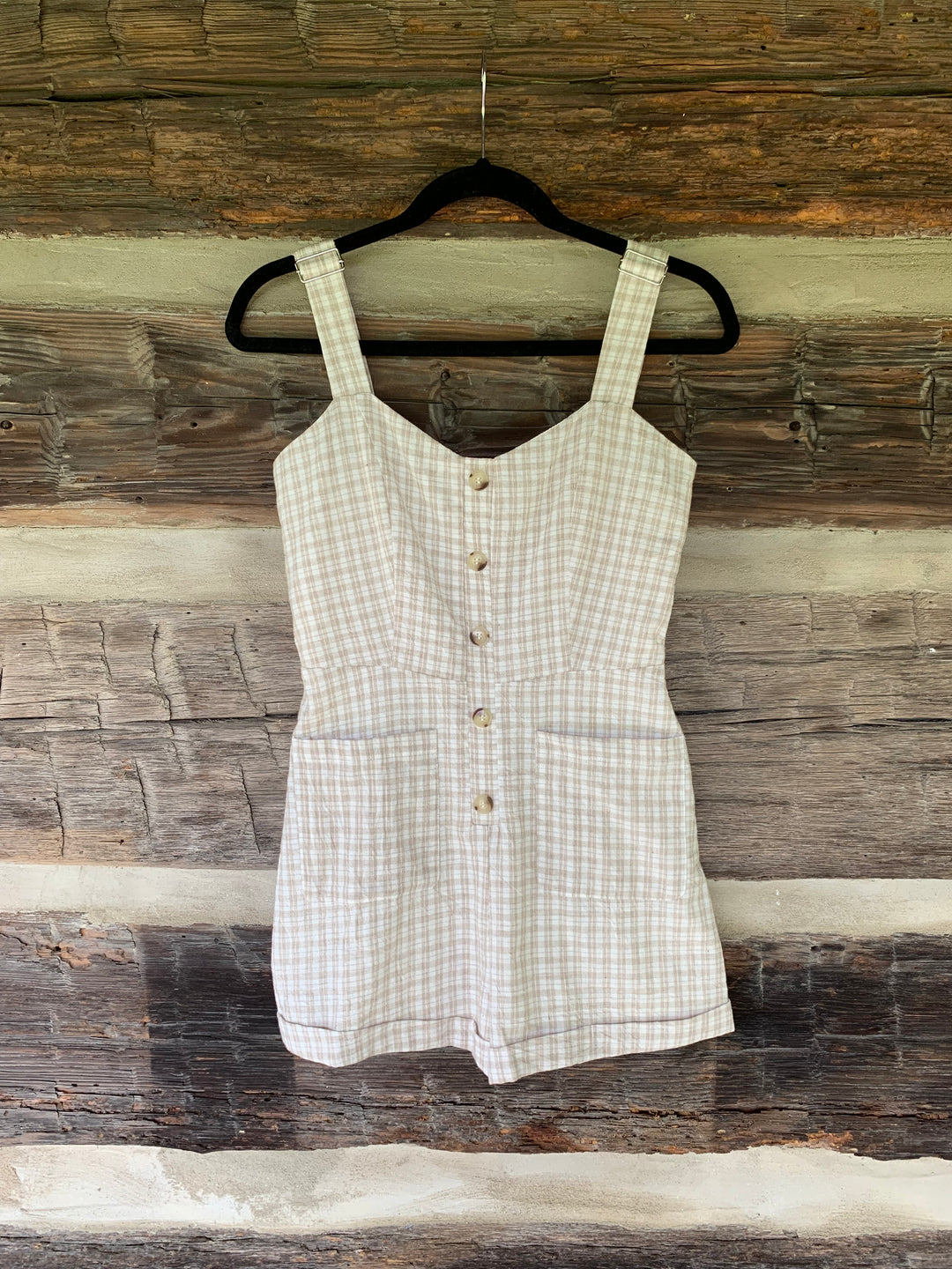 White checkered romper on a hanger against a wooden background
