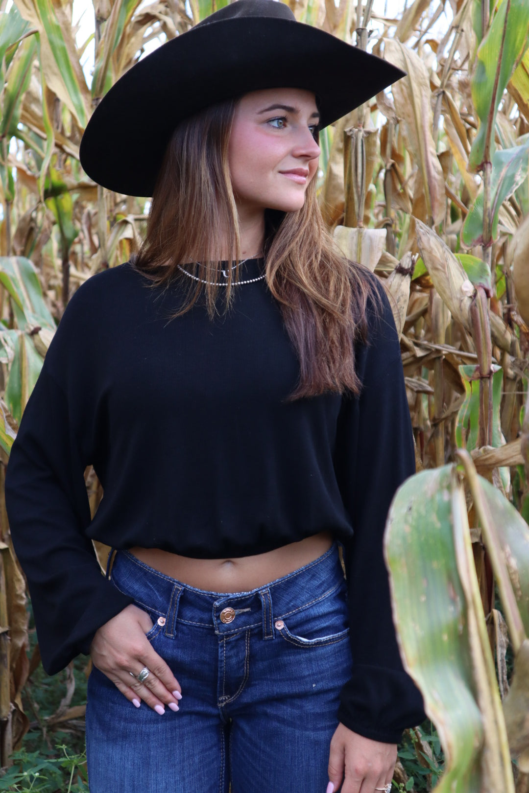Person wearing a black hat and dark top standing in a field of tall grass.