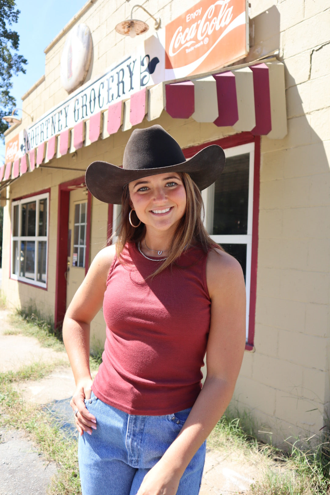 Woman wearing a cowboy hat in front of a building with a Coca-Cola sign.