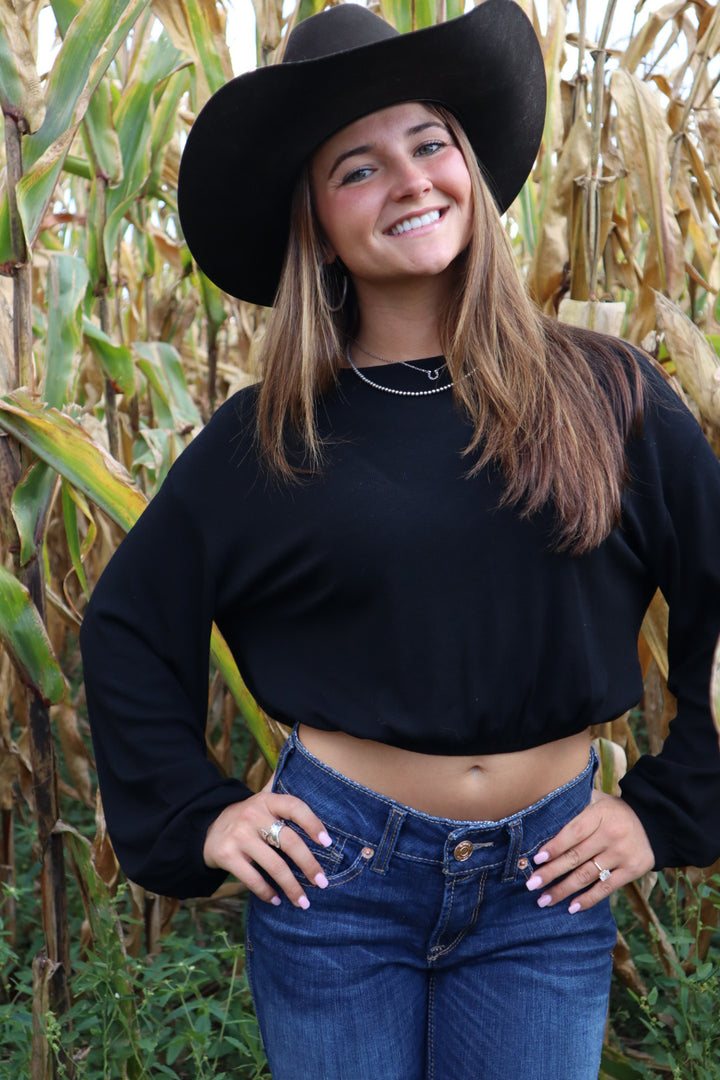 Woman wearing a black top and wide-brimmed hat standing in a cornfield
