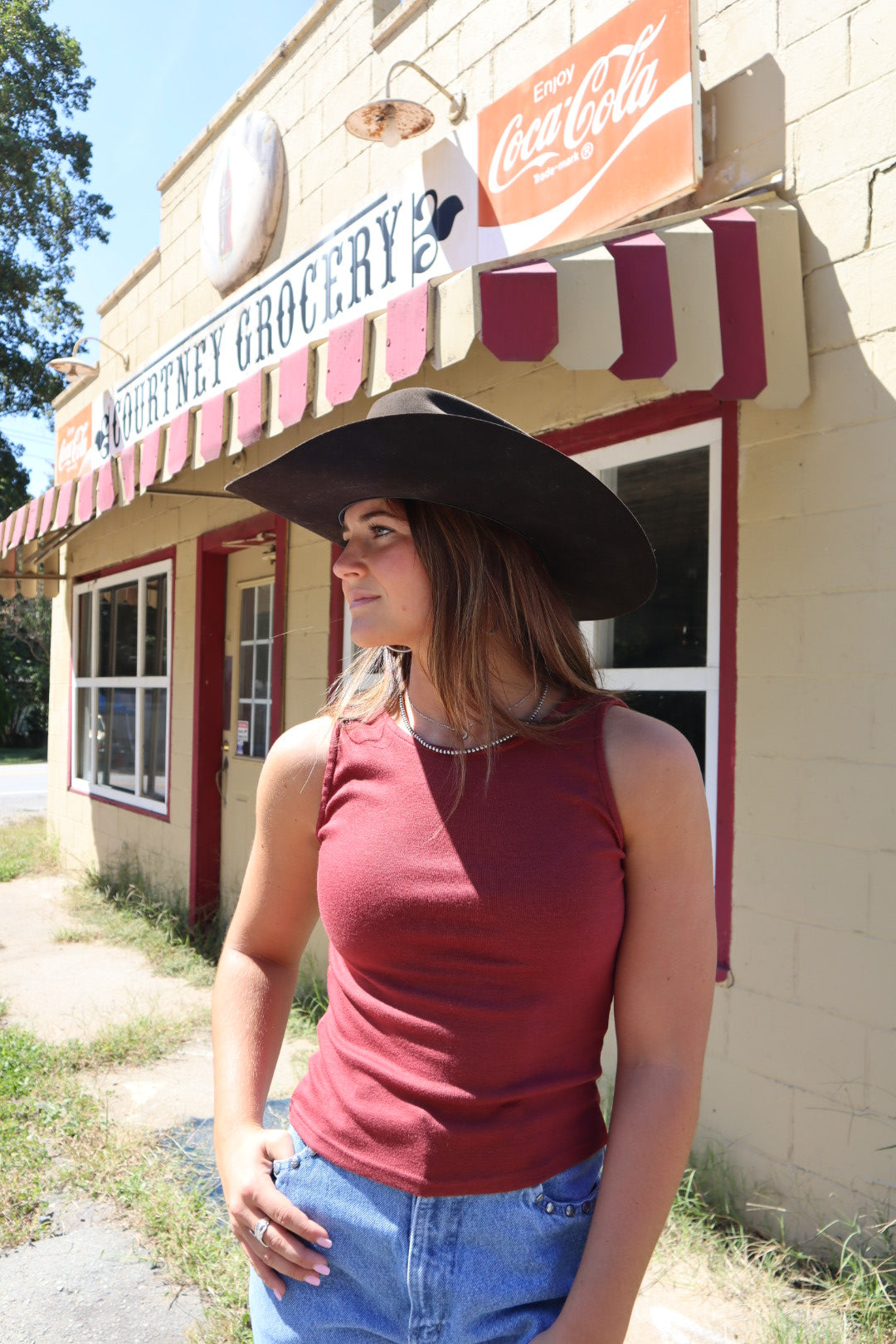 Woman wearing a cowboy hat and red shirt standing in front of a building with a Coca-Cola sign.