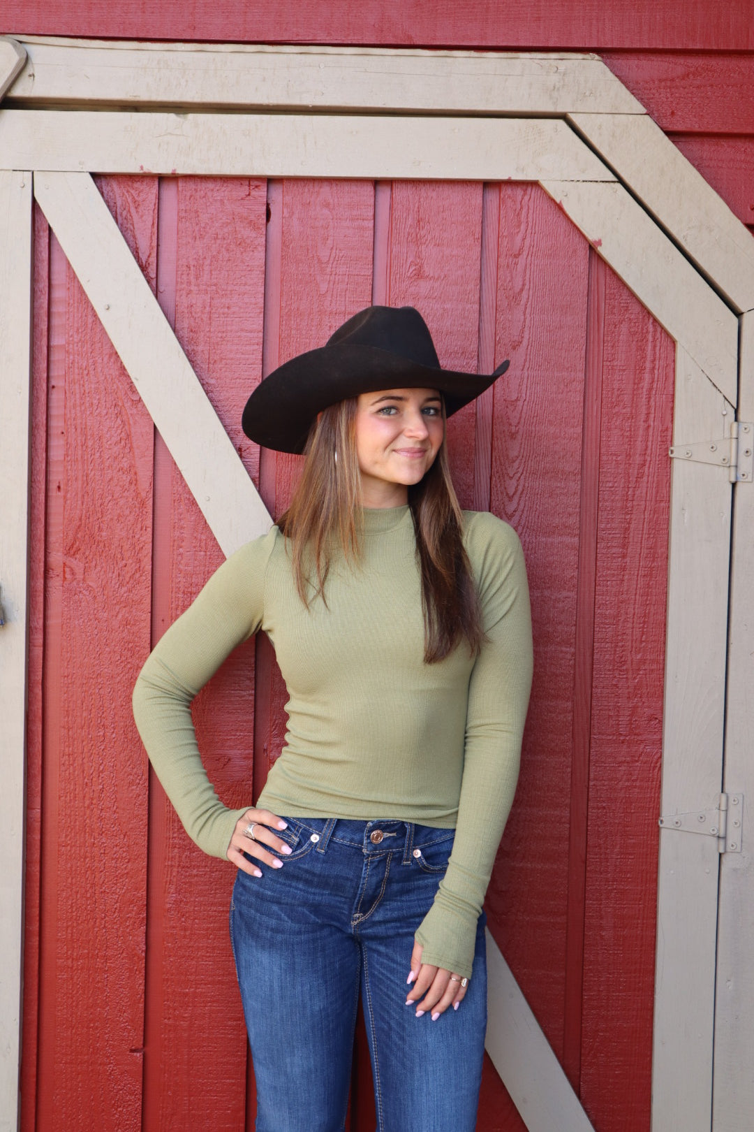 Woman wearing a green long-sleeve top and blue jeans against a red wooden background