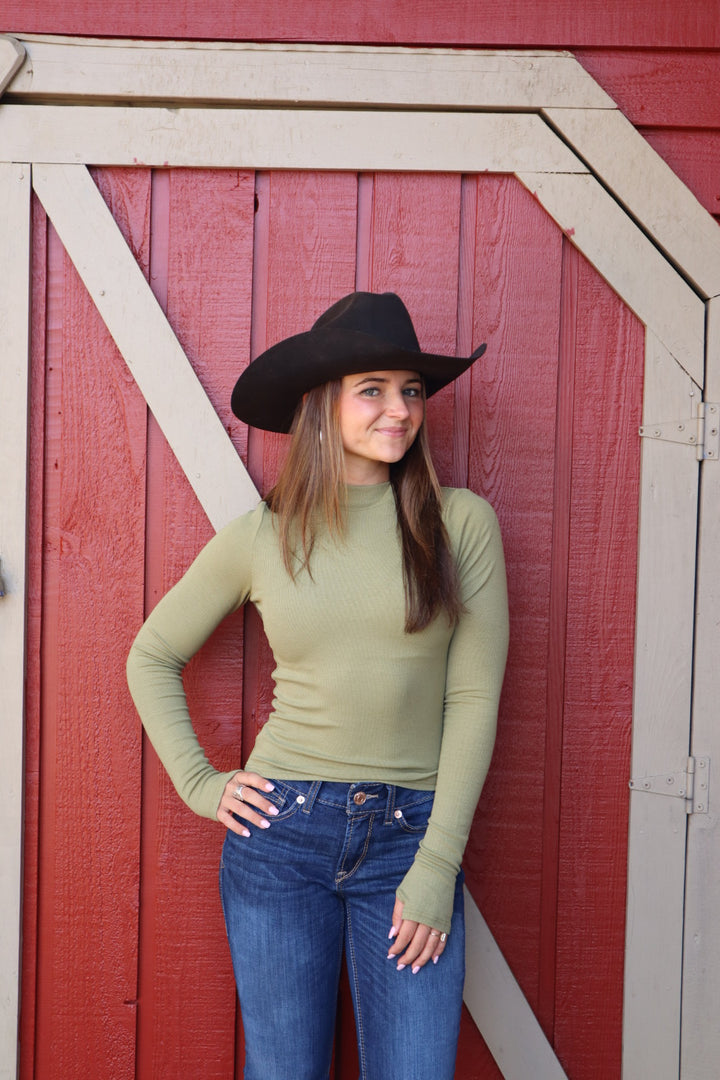 Woman wearing a green long-sleeve top and blue jeans against a red wooden background