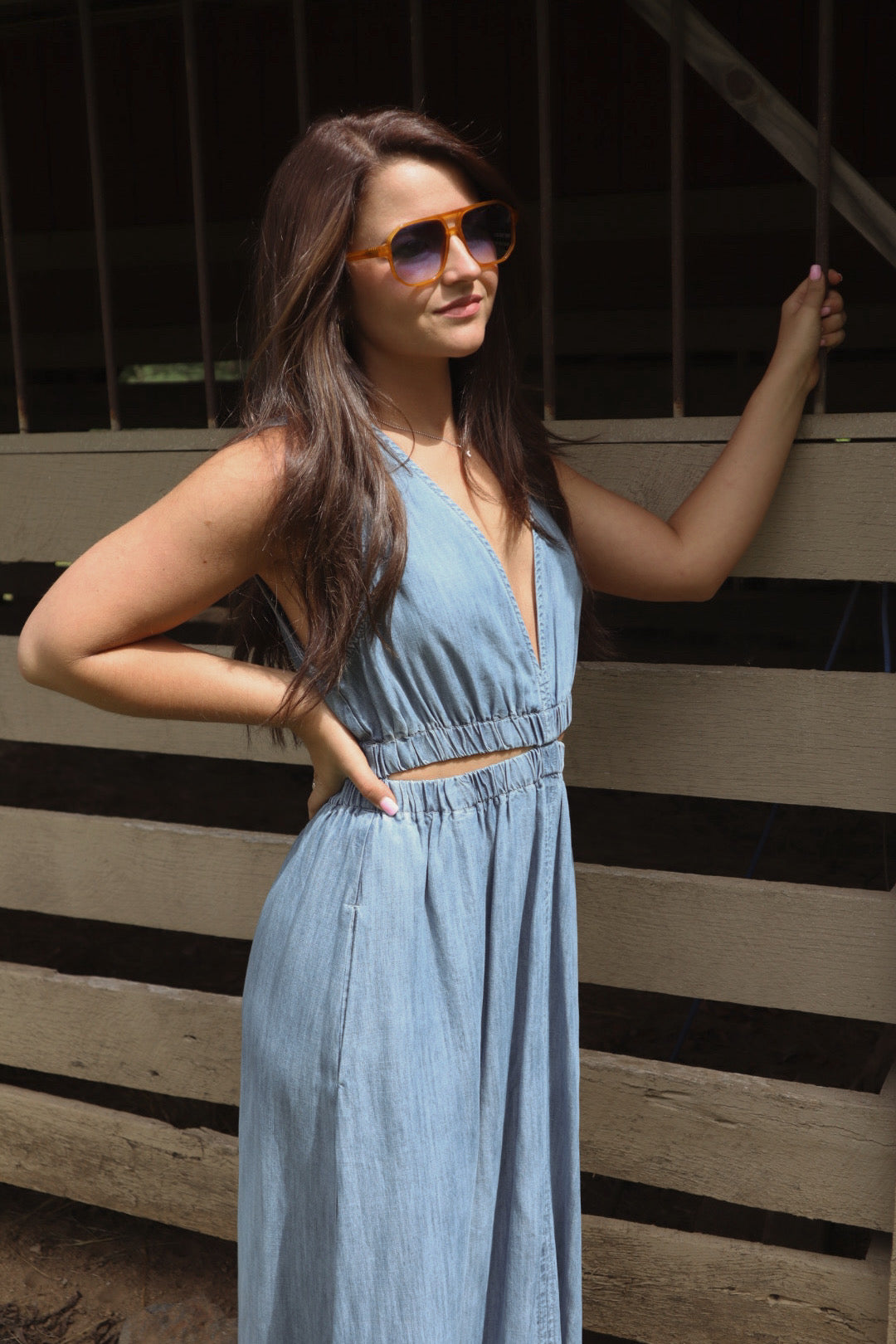 Woman in a blue dress and sunglasses standing against a striped wall.