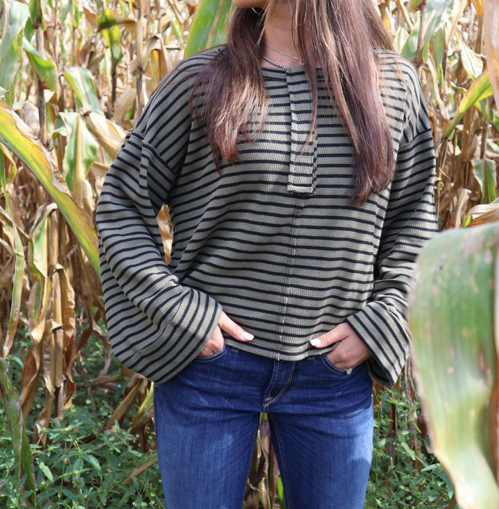 Person wearing a striped sweater and blue jeans standing in a cornfield