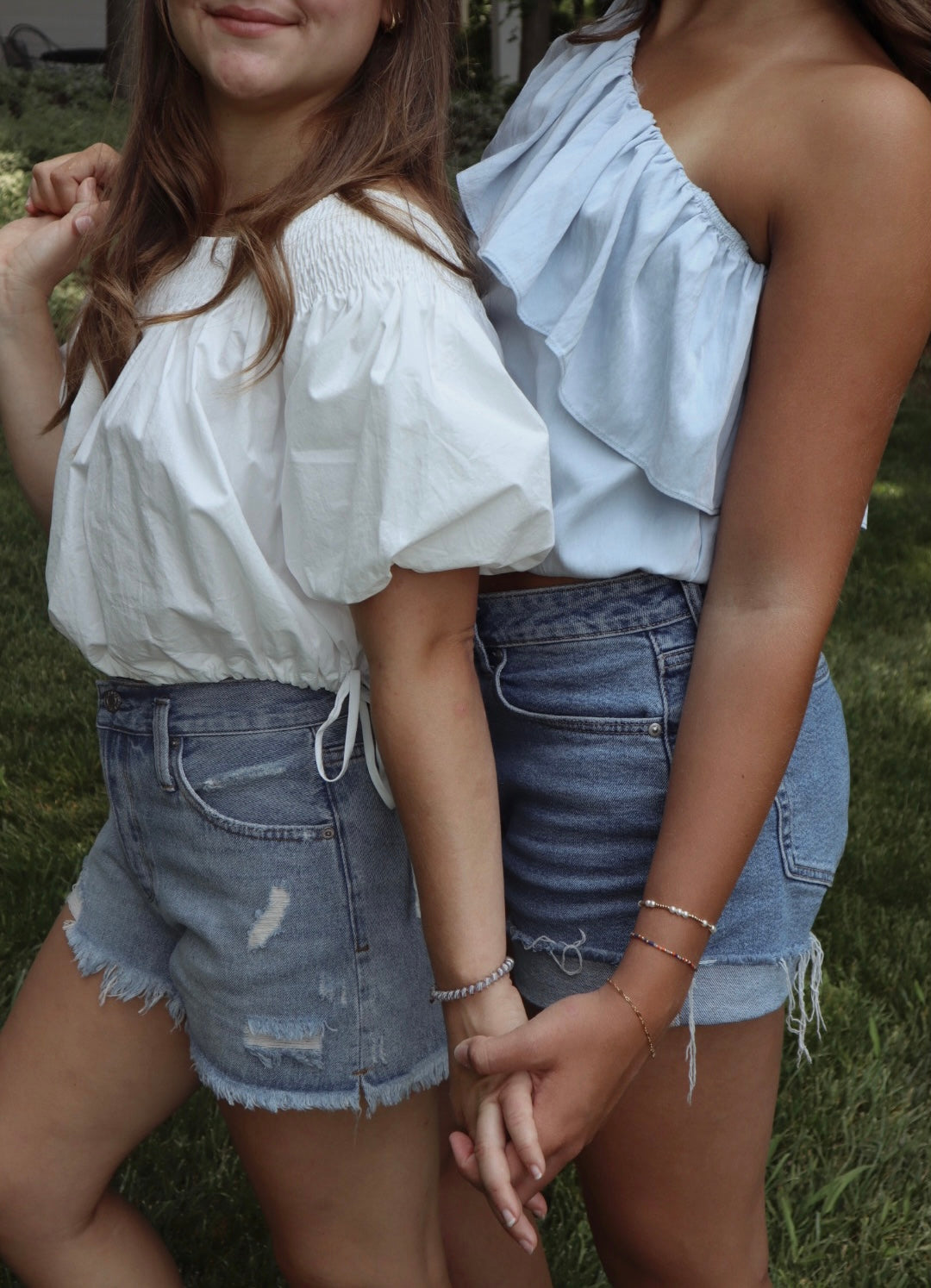 Two women wearing white tops and denim shorts standing close together outdoors.